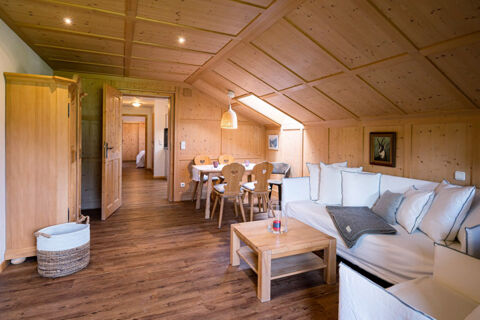 Living area with wooden walls, ceiling, and floor, white sofa, dining table with chairs, and a basket at Landhaus Berktold