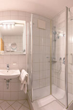 Bathroom at Landhaus Berktold with white tiled walls, a glass shower enclosure, sink, and a mirror with lights above it