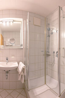 Bathroom at Landhaus Berktold with white tiled walls, a glass shower enclosure, sink, and a mirror with lights above it