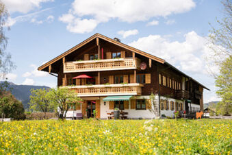 Rustic wooden chalet-style building with balconies and flower boxes surrounded by a blooming field at Landhaus Berktold