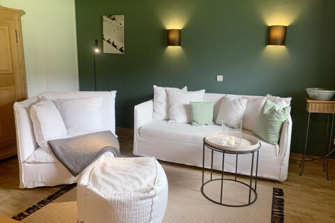 Living room at Landhaus Berktold with white sofas, cushions, a small round table, and dark green walls with lights