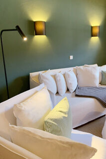 White sectional sofa with multiple pillows and gray blanket under two wall lights and a standing lamp at Landhaus Berktold