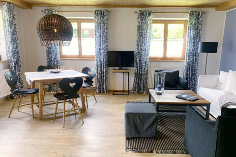 Spacious living room at Landhaus Berktold with wooden dining table, heart-back chairs, white sofa, and patterned curtains on windows