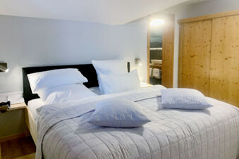 A neatly made double bed with white pillows and quilted bedding in a room at Landhaus Berktold with wood accents and soft lighting