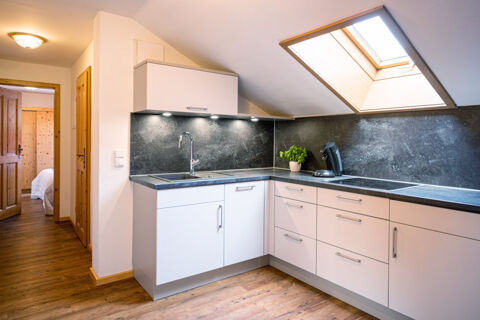 Modern kitchen interior at Landhaus Berktold with white cabinets, black countertops, skylight, and wood flooring visible through open doors