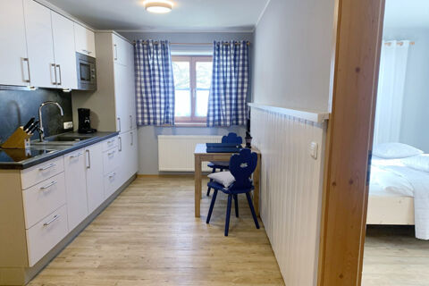 Kitchen area with white cabinets, wooden floor, blue checkered curtains, and a small dining table with chairs at Landhaus Berktold