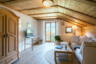 Living room with wooden ceiling and floor, sofa, armchair, TV on a table, and balcony at Landhaus Berktold