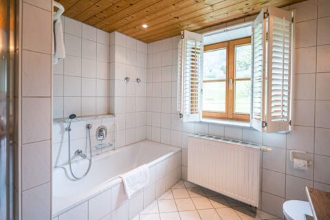 Bathroom at Landhaus Berktold featuring a white tiled bathtub with a handheld shower, wooden ceiling, and window shutters open to a countryside view