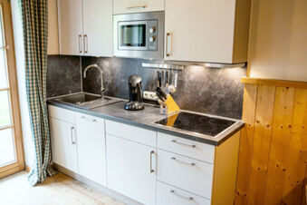 Modern kitchen in Landhaus Berktold with white cabinets, built-in microwave, electric stovetop, sink, and coffee maker near a window with checked curtains