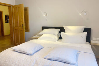 A neatly made bed with multiple white pillows and a duvet in a room at Landhaus Berktold with wooden doors and floor visible