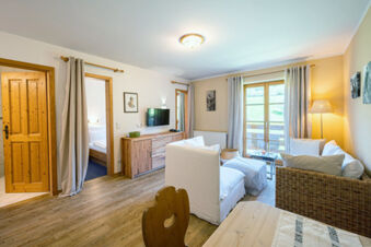Living area at Landhaus Berktold with wicker and white sofas, wooden furniture, large window with curtains, and soft lighting