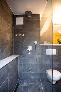 Shower area with dark grey tiles, silver showerheads, controls, a white toilet, and part of a wooden door at Landhaus Berktold
