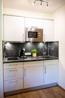 Modern kitchen in Landhaus Berktold with white cabinets, stainless steel microwave, black countertop, coffee maker, and a sink with faucet