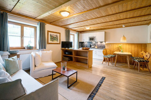 Bright living room with wooden ceiling, white sofa, armchair, kitchen area, and dining table in Landhaus Berktold