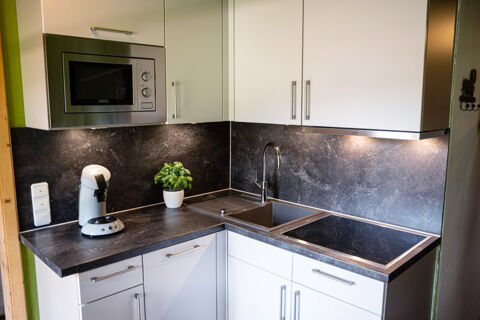 Modern kitchen corner at Landhaus Berktold with white cabinets, black countertop, sink, stove, microwave, coffee machine, and plant
