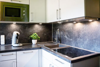 Modern kitchen corner at Landhaus Berktold with white cabinets, microwave, coffee maker, sink, potted plant, and stovetop