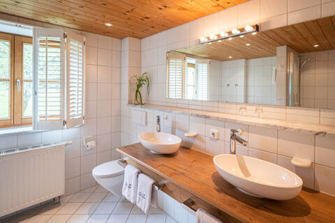 Bathroom interior at Landhaus Berktold with wooden ceiling, twin vessel sinks on a wooden countertop, towel racks, and white tiles