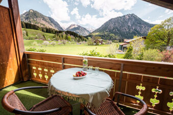 Balcony view at Landhaus Berktold with two wicker chairs, a table with a cloth, strawberries, and mountain scenery in background