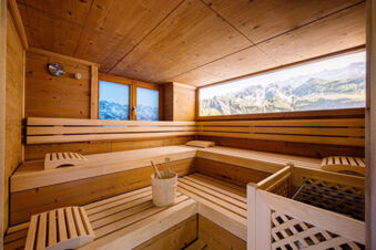 Wood-paneled sauna room at Landhaus Berktold with wooden benches, headrests, bucket with ladles, and window showing mountain view