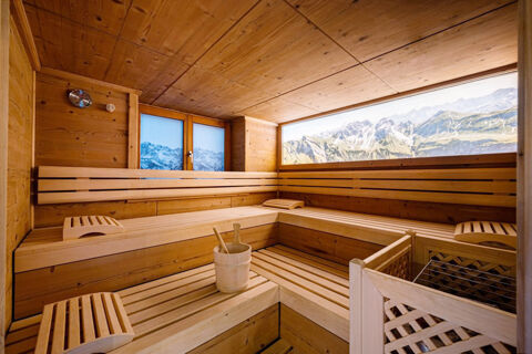 Wood-paneled sauna room at Landhaus Berktold with wooden benches, headrests, bucket with ladles, and window showing mountain view