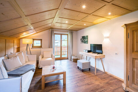 Living room with wooden ceiling, white sofa, armchair, table, TV on stand, and balcony at Landhaus Berktold