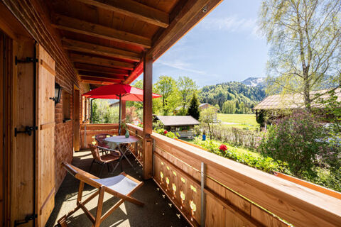 Balcony at Landhaus Berktold with wooden walls, chairs, table with red umbrella, overlooking green landscape and mountains