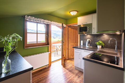 Kitchen interior at Landhaus Berktold with green walls, wooden door, window, black countertops, and a balcony view