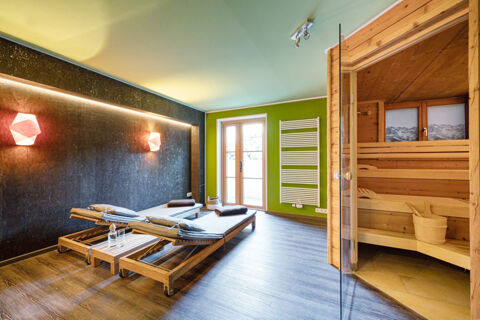 Room with two wooden lounge chairs with cushions, a table with water, wall lights, green wall, and sauna at Landhaus Berktold