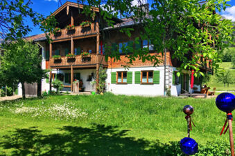 A two-story building with wooden balconies and green shutters surrounded by green grass and trees at Landhaus Berktold