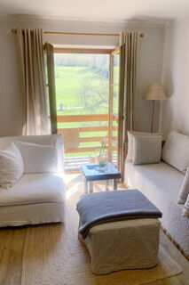 Sunlit seating area at Landhaus Berktold with white and beige sofas, a small table, and an open door to a green view
