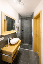 Bathroom at Landhaus Berktold with wooden door, vanity with vessel sink, large mirror, and walk-in shower with glass doors
