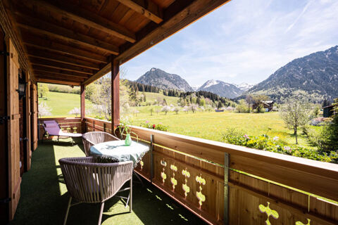 Balcony with wicker chairs and a table covered with a cloth at Landhaus Berktold overlooking a green meadow and mountain range