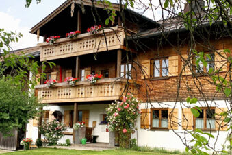 Traditional wooden facade of Landhaus Berktold with balconies adorned by flower pots and green garden in front