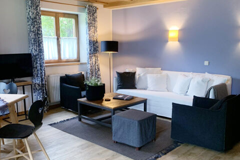 A living room at Landhaus Berktold with a white sofa, black armchairs, wooden coffee table, and patterned curtains near a window