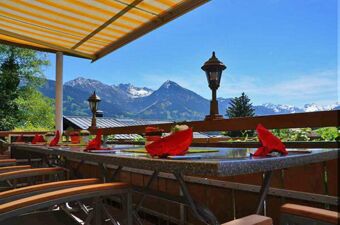 Terrasse mit gedeckten Tischen und Alpenpanorama im Hintergrund beim Panorama-Hotel Kaserer unter blauem Himmel und Sonnenschutz.