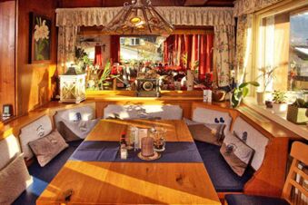 Gem&uuml;tlicher Essbereich mit Holztisch, Kissen und Pflanzen im Sonnenlicht im Panorama-Hotel Kaserer f&uuml;r entspannte Mahlzeiten.