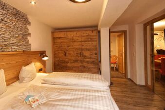 Gem&uuml;tliches Hotelzimmer mit Doppelbett, Holzschrank und Steinwanddekor im Panorama-Hotel Kaserer, warm eingerichteter Raum.