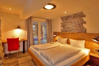 Gem&uuml;tliches Doppelzimmer im Panorama-Hotel Kaserer mit Holzm&ouml;beln, Steindekoration &uuml;ber dem Bett und Blick auf den Balkon.