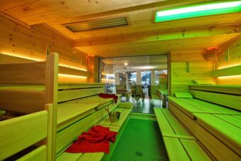 Innenansicht einerholzvert&auml;felten Sauna mit Sitzb&auml;nken, roten Handt&uuml;chern und Blick durch Glas auf einen Ruheraum im Panorama-Hotel Kaserer.