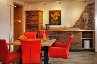 Ein Essbereich mit roten St&uuml;hlen, Holztisch und rustikalen Holzschr&auml;nken im Panorama-Hotel Kaserer, dekoriert mit einem Blumenbild.