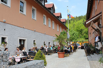 Outdoor seating area with people dining between two orange and gray buildings at Landgasthof Hotel Hammerm&uuml;hle with greenery nearby