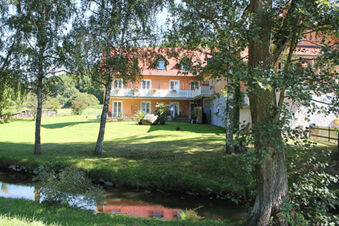 Landgasthof Hotel Hammerm&uuml;hle building with orange walls and red roof surrounded by trees and a small stream in front