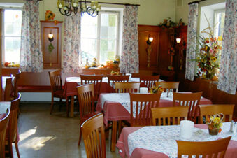 Dining area in Landgasthof Hotel Hammerm&uuml;hle with wooden chairs, tables covered in pink and floral tablecloths, and floral curtains