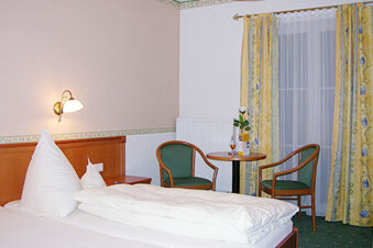 Single bed with white bedding and pillows next to two green cushioned chairs and a round table in Landgasthof Hotel Hammerm&uuml;hle room