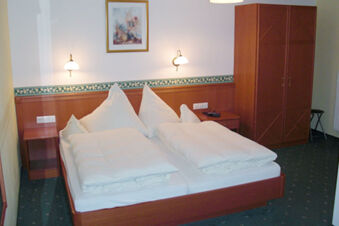 A double bed with white pillows and duvets is centered between two wooden nightstands under wall lamps in Landgasthof Hotel Hammerm&uuml;hle