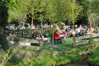 Outdoor dining area with people seated at tables under trees near a creek at Landgasthof Hotel Hammerm&uuml;hle