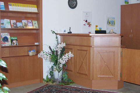 Reception desk with floral arrangement, informational brochures on shelves, and clock on white wall at Landgasthof Hotel Hammerm&uuml;hle