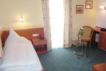Single bed with white bedding next to a nightstand and curtains, a glass table with a flower, and a chair at Landgasthof Hotel Hammerm&uuml;hle