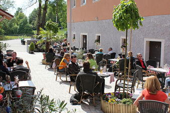 Outdoor seating area with people dining and drinking at tables along the building wall of Landgasthof Hotel Hammerm&uuml;hle