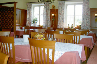 Wooden chairs and tables with floral tablecloths in a dining room of Landgasthof Hotel Hammerm&uuml;hle with floral curtains and decorations
